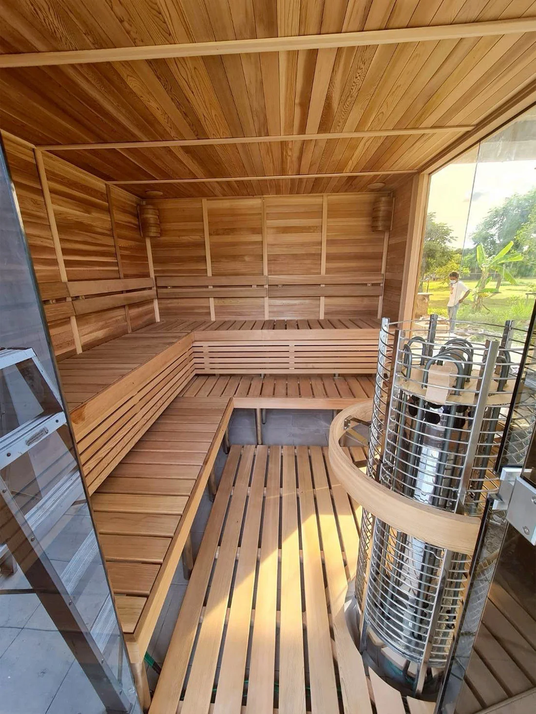 Cedar sauna interior with a tower heater and a garden view through glass